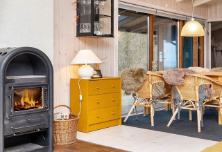 Gezellige hoek in vakantiehuis in Knebel, Denemarken, met houtkachel, gele kast en rieten stoelen.