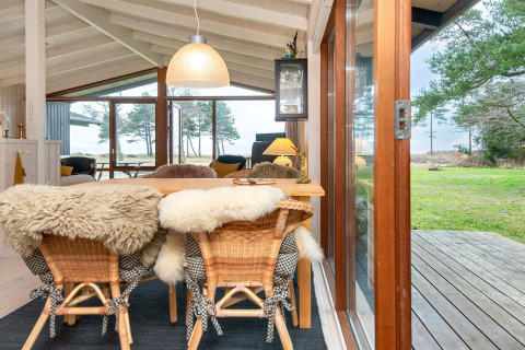 Espace repas chaleureux avec chaises en peau et grandes fenêtres dans la maison de vacances à Knebel, Danemark.