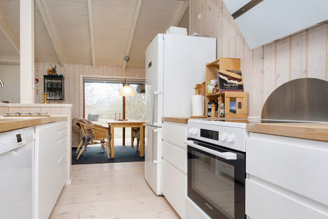 Moderne keuken en eetruimte in een vakantiewoning in Knebel, Denemarken, met licht hout en witte toestellen.