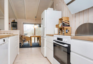 Cuisine moderne et coin repas dans une maison de vacances à Knebel, Danemark, avec bois clair et électroménagers blancs.