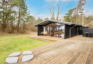 Casa vacanze in legno con ampia terrazza e sedute esterne, immersa nel verde a Knebel, Danimarca.