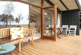 Træterrasse med åbent dørparti, havemøbler og udsigt til naturen ved 4-personers feriehus i Knebel, Danmark.