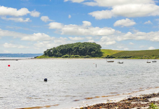 Uitzicht op een rustige kust met boten en een groen eiland bij Knebel, Denemarken op een zonnige dag.
