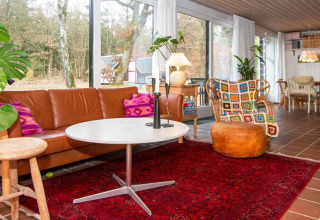 Woonkamer in vakantiehuis in Ebeltoft, Denemarken met leren zetel, kleurrijke kussens en grote ramen.