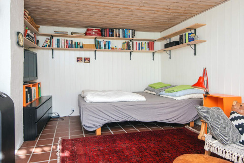 Chambre chaleureuse avec étagères de livres, lit double, tapis rouge et plafond en bois à Ebeltoft, Danemark.