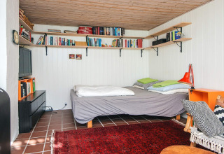 Knusse slaapkamer met boekenplanken, dubbel bed en rood tapijt in een lodge in Ebeltoft, Denemarken.