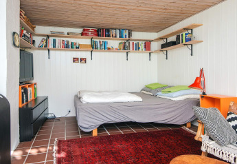 Chambre chaleureuse avec étagères de livres, lit double, tapis rouge et plafond en bois à Ebeltoft, Danemark.
