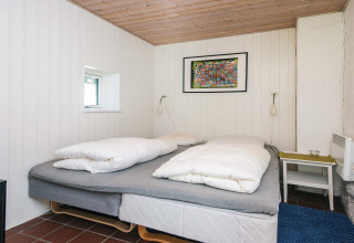 Slaapkamer met tweepersoonsbed, witte houten wanden, houten plafond en kleurig kunstwerk in Ebeltoft, Denemarken.