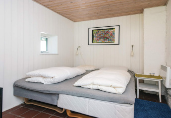 Slaapkamer met tweepersoonsbed, witte houten wanden, houten plafond en kleurig kunstwerk in Ebeltoft, Denemarken.