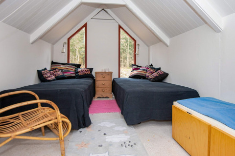 Zolderkamer met twee eenpersoonsbedden, kleurrijke kussens en boszicht in vakantiehuis in Ebeltoft, Denemarken.