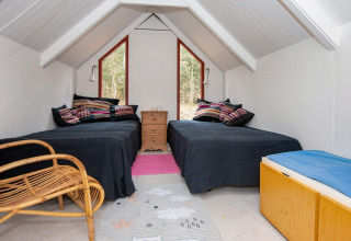Zolderkamer met twee eenpersoonsbedden, kleurrijke kussens en boszicht in vakantieverblijf Ebeltoft, Denemarken.