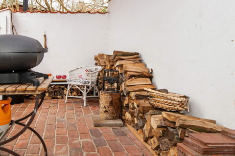 Buitenhoek met stapels haardhout, barbecue en witte rotan stoelen op een bakstenen vloer in Ebeltoft.