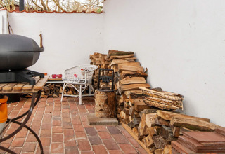 Terrasse extérieure avec bois empilé, barbecue et mobilier en osier blanc sur sol en briques à Ebeltoft.