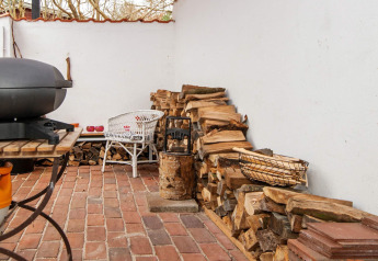 Außenbereich mit gestapeltem Brennholz, Grill und weißen Gartenmöbeln auf Ziegelboden in Ebeltoft.