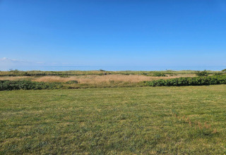 View from a lodge overlooking a grassy field, wild shrubs, and a clear blue sky extending into the distance.