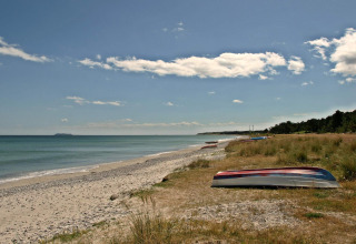 Ruhiger Strand mit umgedrehten Booten, Kies, Meer und leicht bewölktem Himmel in naturnaher Umgebung.
