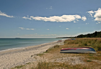 Ruhiger Strand mit umgedrehten Booten, Kies, Meer und leicht bewölktem Himmel in naturnaher Umgebung.