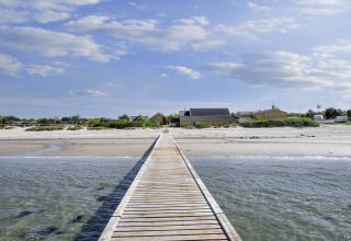 Wooden walkway leading to a yellow holiday home on the beach in Glesborg, Denmark, under blue sky.