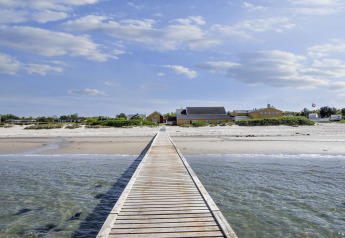 Pasarela de madera hacia casa de vacaciones amarilla en la playa de Glesborg, Dinamarca y cielo azul.