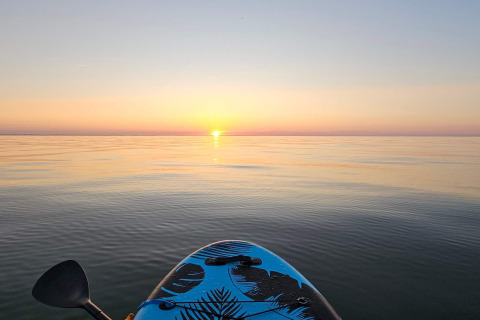 Serene sunset view from a kayak on calm water at a lodge, with a visible paddle in the foreground.