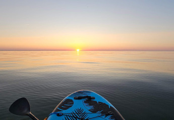 Vista de una tranquila puesta de sol desde un kayak sobre aguas calmas en un alojamiento, remo visible.
