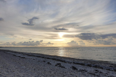 Sunset view over a calm sea and sandy beach with clouds, photographed from a lodge by the shore.