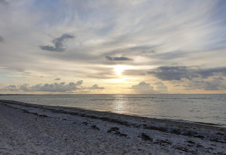 Sunset view over a calm sea and sandy beach with clouds, photographed from a lodge by the shore.
