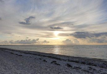 Vista de la puesta de sol sobre el mar tranquilo y playa, tomada desde un lodge con cielo nublado.