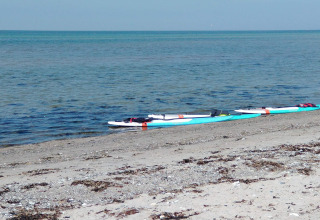 Dos tablas de paddle surf reposan en una playa de piedras junto al mar en un lodge, bajo cielo azul.