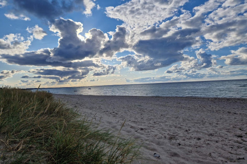 Zandstrand en grasduinen met dramatische wolkenlucht in Glesborg, Denemarken, bij een vakantiehuisje.