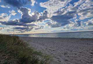 Sandy beach and grassy dunes under dramatic clouds by the sea in Glesborg, Denmark, near a holiday home.