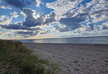 Zandstrand en grasduinen met dramatische wolkenlucht in Glesborg, Denemarken, bij een vakantiehuisje.