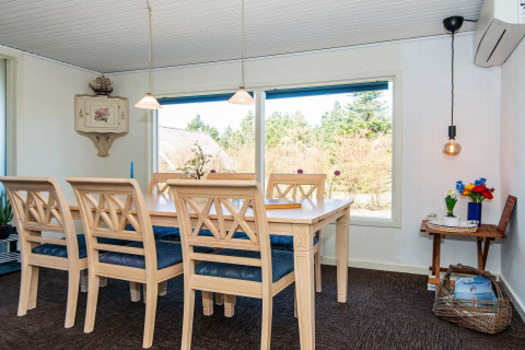 Dining area with large table, six chairs and scenic window view at 6 person holiday home in Glesborg, Denmark.