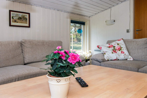 Cozy living room in Glesborg holiday lodge with beige sofa, floral décor, remote and window view.