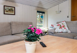 Cozy living room in Glesborg holiday lodge with beige sofa, floral décor, remote and window view.