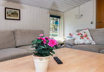 Acogedora sala de estar en casa de vacaciones en Glesborg con sofá, flores y control remoto en mesa.