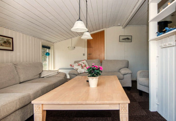 Salon lumineux d’une maison de vacances à Glesborg, Danemark, avec canapés, table basse et plante.