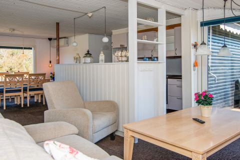Acogedora sala de estar en casa de vacaciones con sofá, silla, mesa de comedor y cocina en Glesborg, Dinamarca.