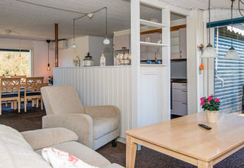 Acogedora sala de estar en casa de vacaciones con sofá, silla, mesa de comedor y cocina en Glesborg, Dinamarca.