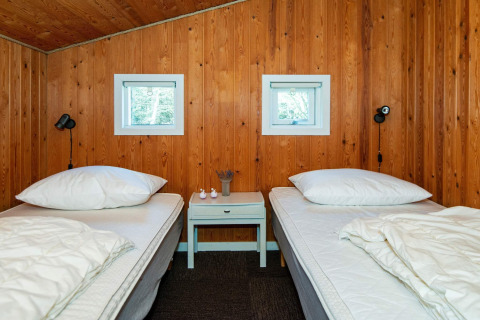 Slaapkamer met twee aparte bedden, houten wanden, kleine vensters en nachtkastje in Glesborg, Denemarken.