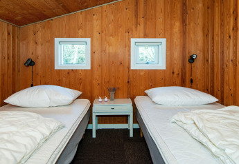 Slaapkamer met twee eenpersoonsbedden, houten muren, kleine ramen en nachtkastje in Glesborg, Denemarken.