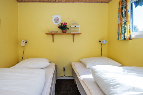 Twee enkele bedden in een knusse gele slaapkamer met wanddecoratie in Glesborg, Denemarken.