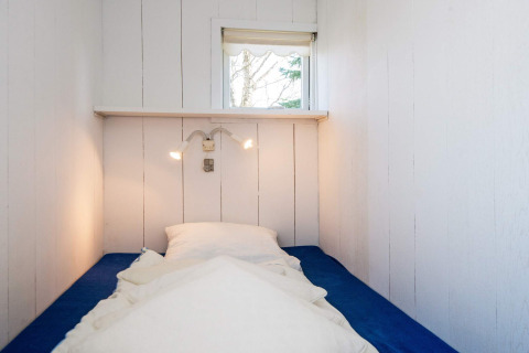 Narrow bedroom with single bed, blue mattress, white pillows, wall lamps and window at Glesborg lodge.