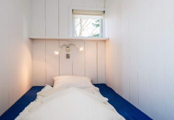 Dormitorio estrecho con cama individual, colchón azul, almohadas blancas, lámparas de pared y ventana en Glesborg.