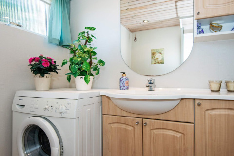 Bright bathroom in a holiday home in Glesborg, Denmark, featuring washing machine, plants, and wood cabinets.