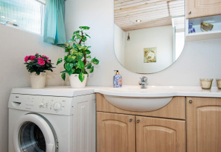 Bright bathroom in a holiday home in Glesborg, Denmark, featuring washing machine, plants, and wood cabinets.