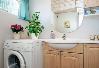 Baño luminoso en una casa de vacaciones en Glesborg, Dinamarca, con lavadora, plantas y muebles de madera.