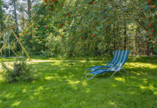 Garden with a lounge chair under a tree, swing set in the background at a holiday home in Glesborg, Denmark.