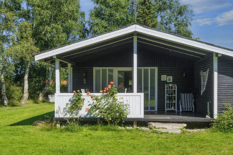 Charming holiday lodge in Glesborg, Denmark, with a porch and garden, surrounded by lush green trees.