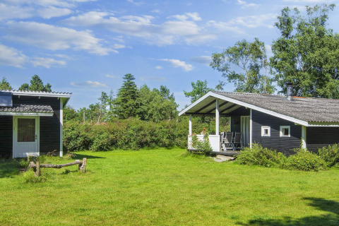 6 person holiday home in Glesborg, Denmark, with green lawn, terrace and lush trees under blue sky.